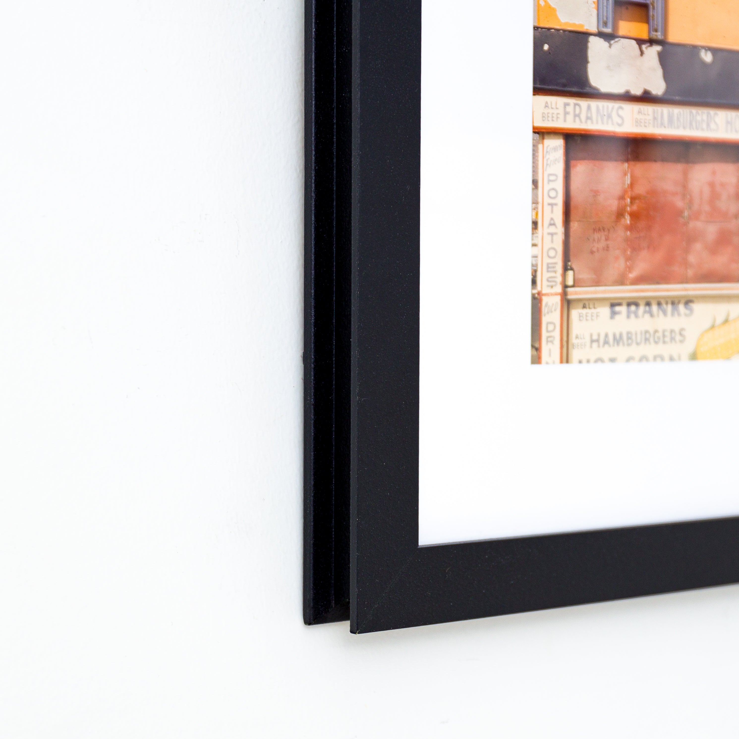 bottom left corner of photo of a sign on a building framed in I-beam style black Williamsburg frame with a white mat