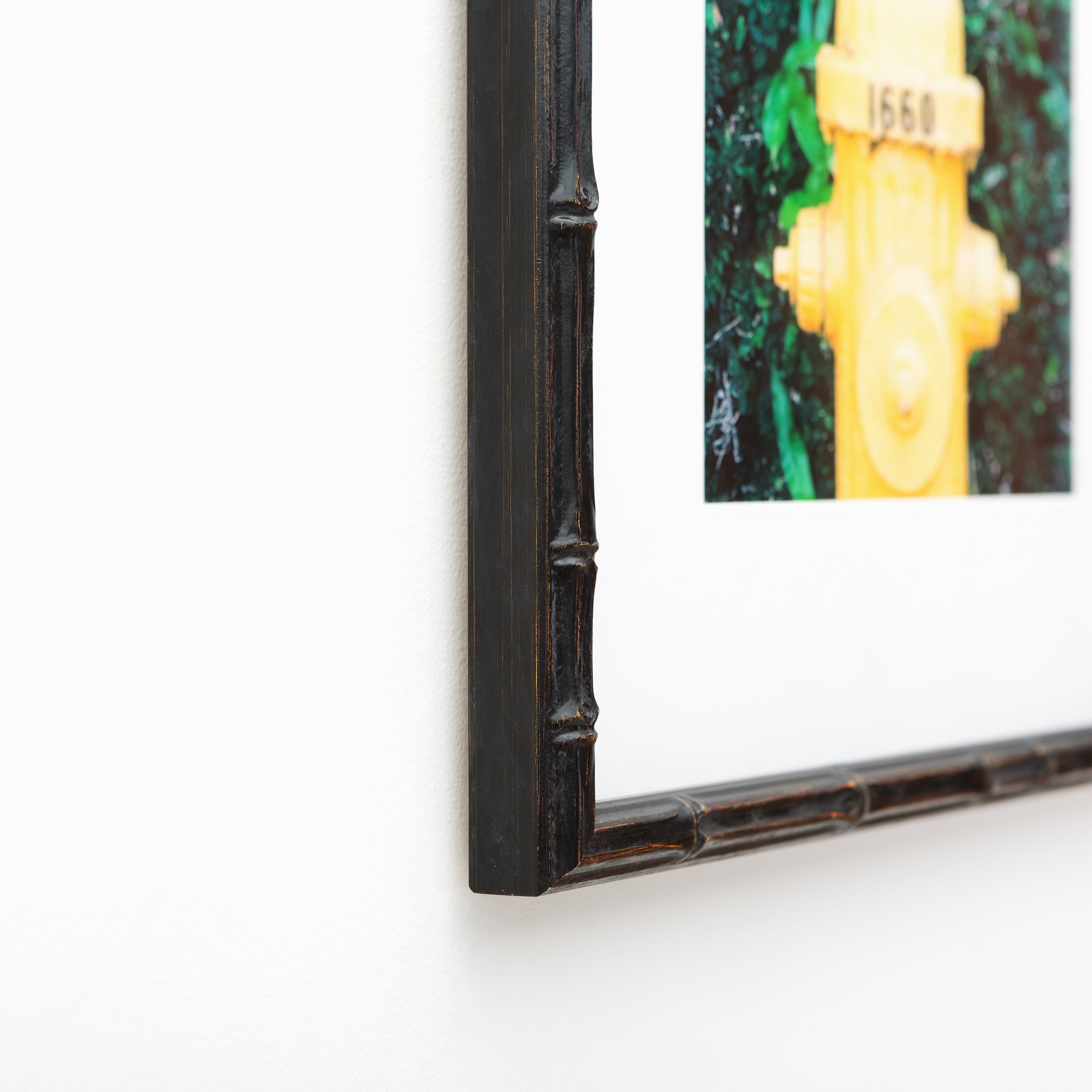bottom left corner of Photo of a yellow fire hydrant framed in a black bamboo Bali frame with a white mat