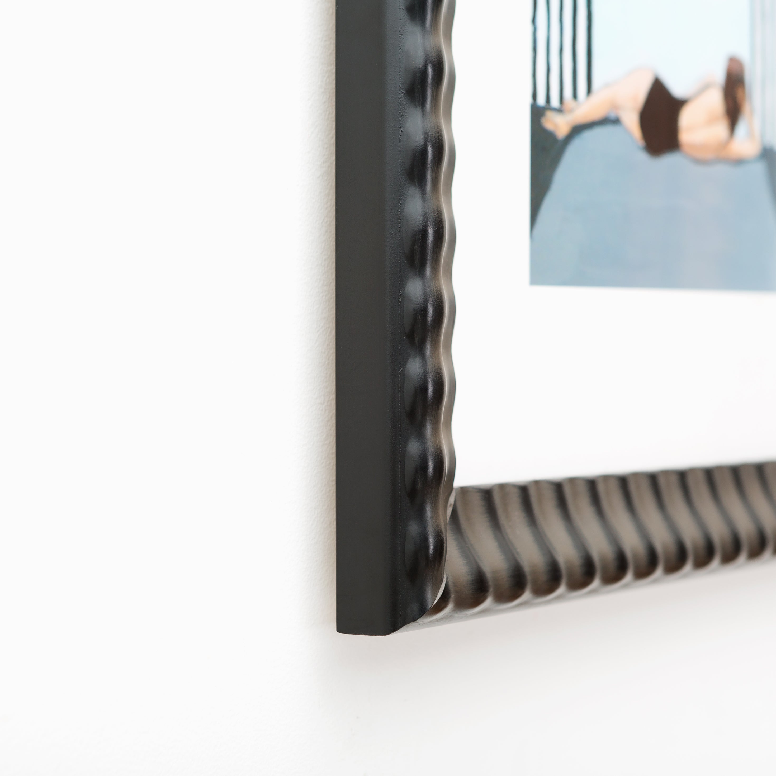 bottom left corner of abstract photo of a woman lounging in a black bathing suit framed in rippled Rialto frame with a white mat