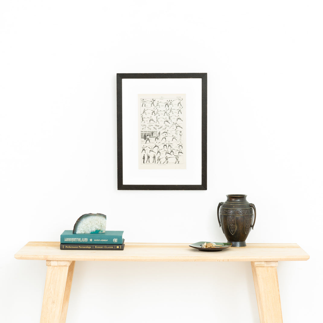 diagram explaining fencing positions framed in Wren distressed matte black finish with aged patina frame with a white mat hanging on a white wall above a wood console table