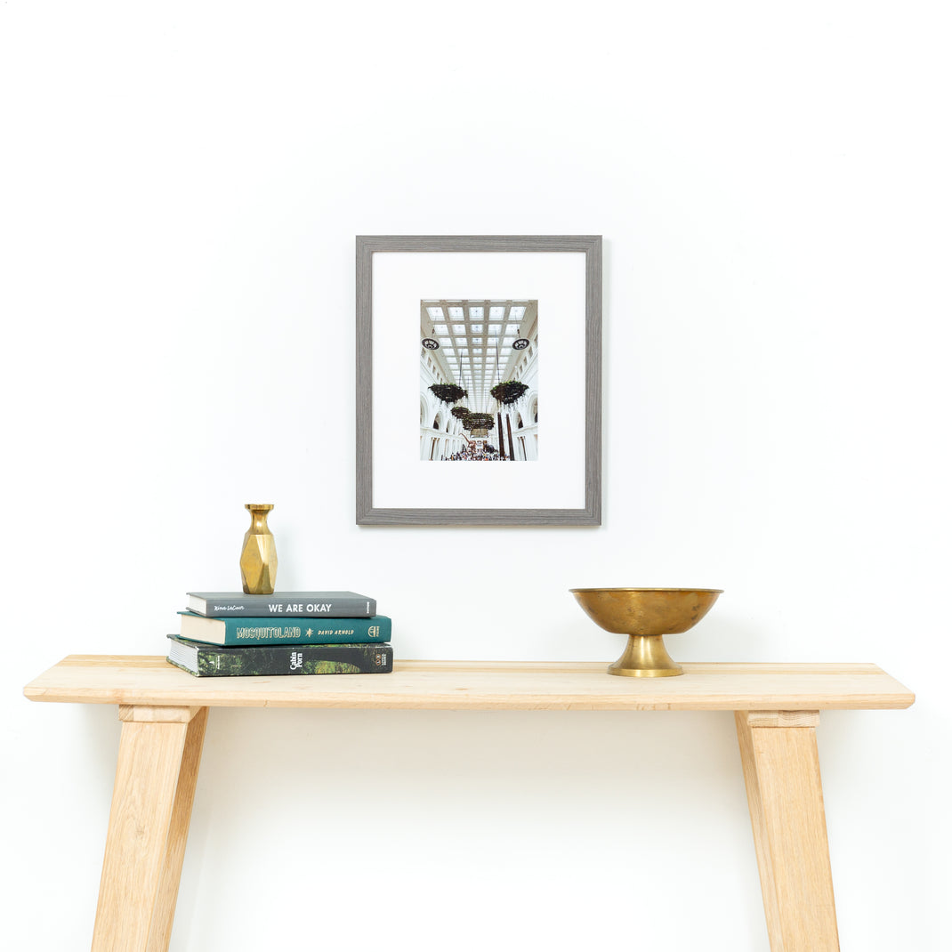 architectural photo of a museum ceiling framed in gray Everett frame with a white mat hanging on a white wall above a light wood console table