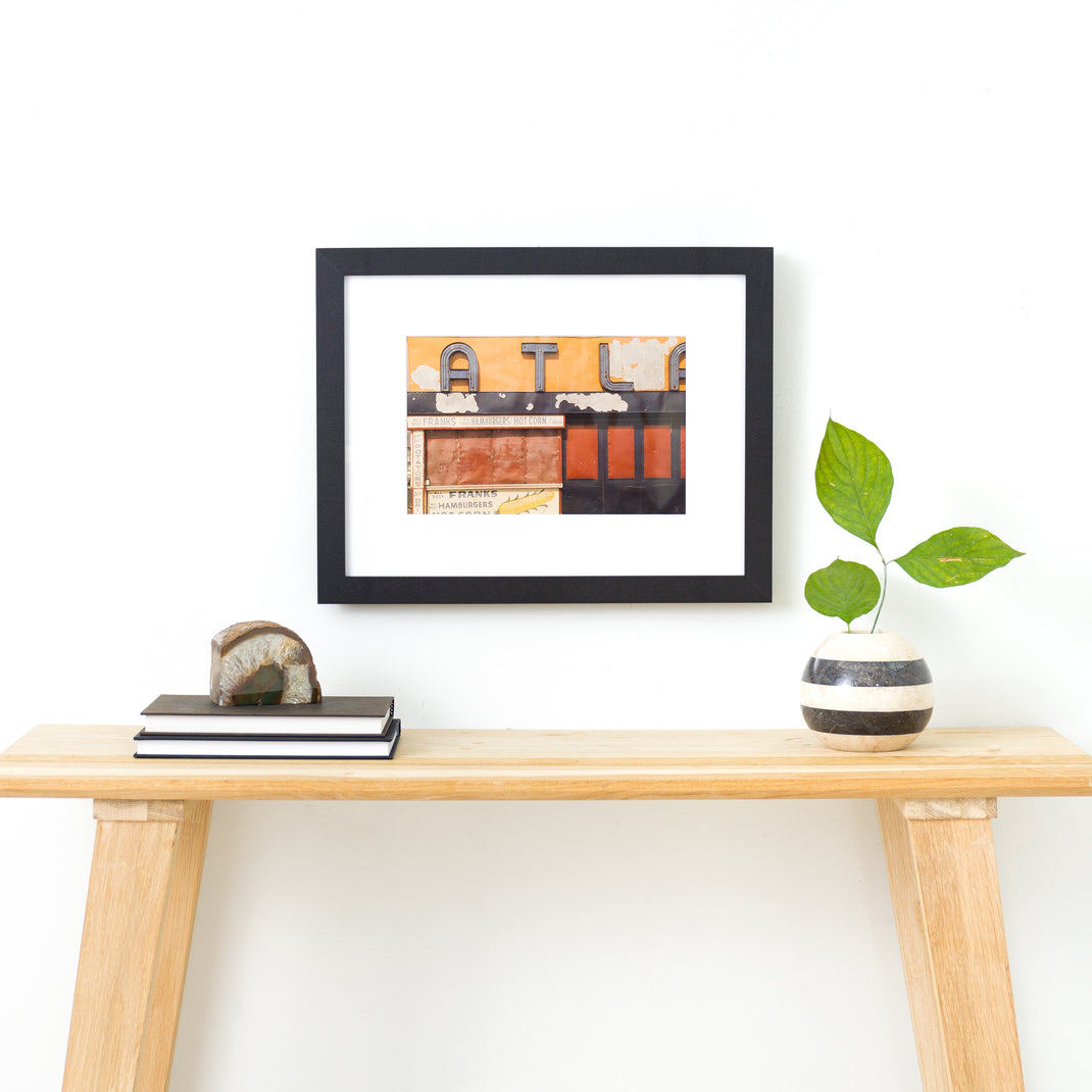 photo of a sign on a building framed in I-beam style black Williamsburg frame with a white mat hanging on a white wall above a wood console table