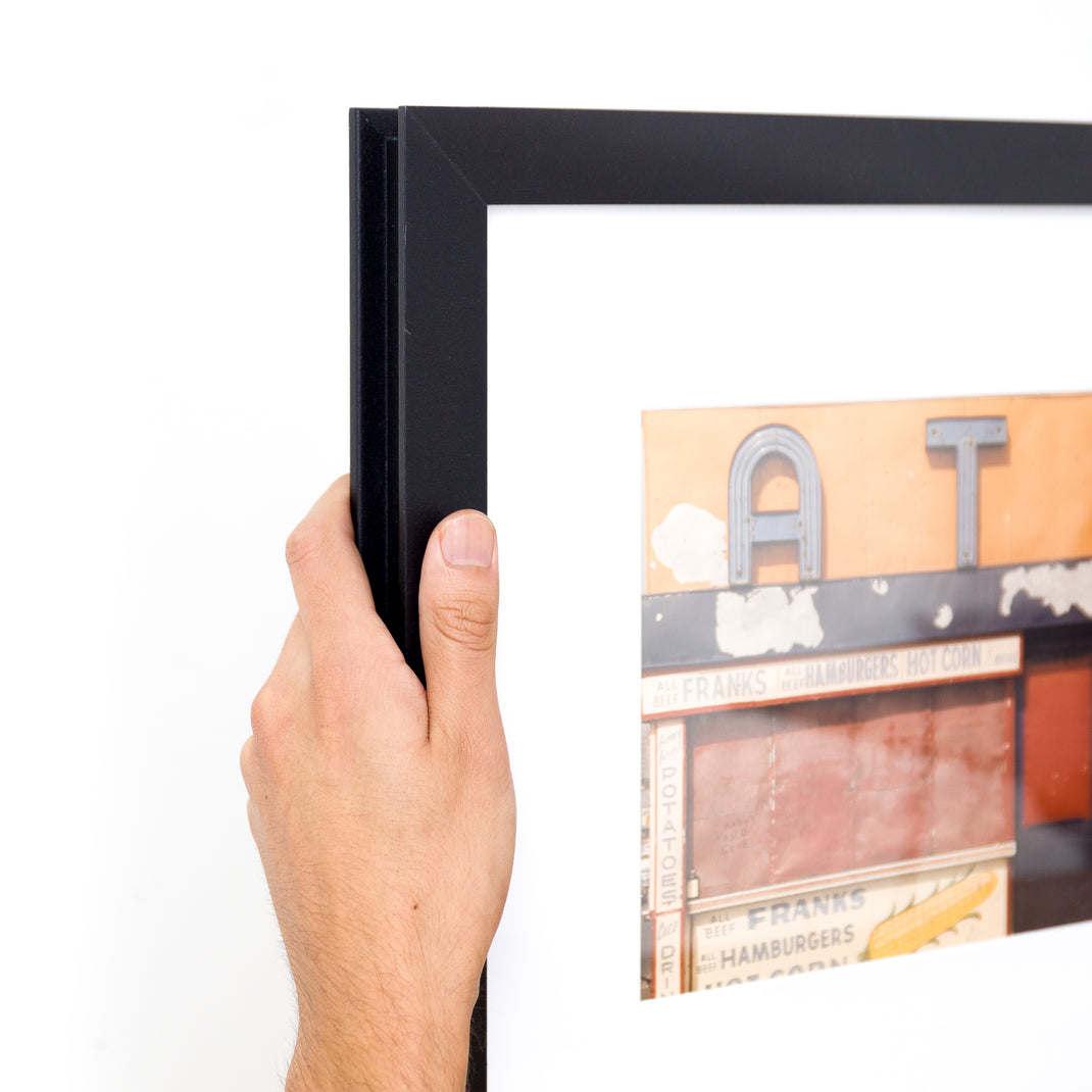 top left corner of photo of a sign on a building framed in I-beam style black Williamsburg frame with a white mat