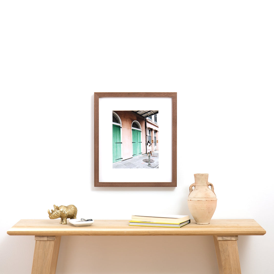 travel photo of a woman exploring framed in Walnut gallery hardwood frame style with a white mat hanging on a white wall above a wood console table