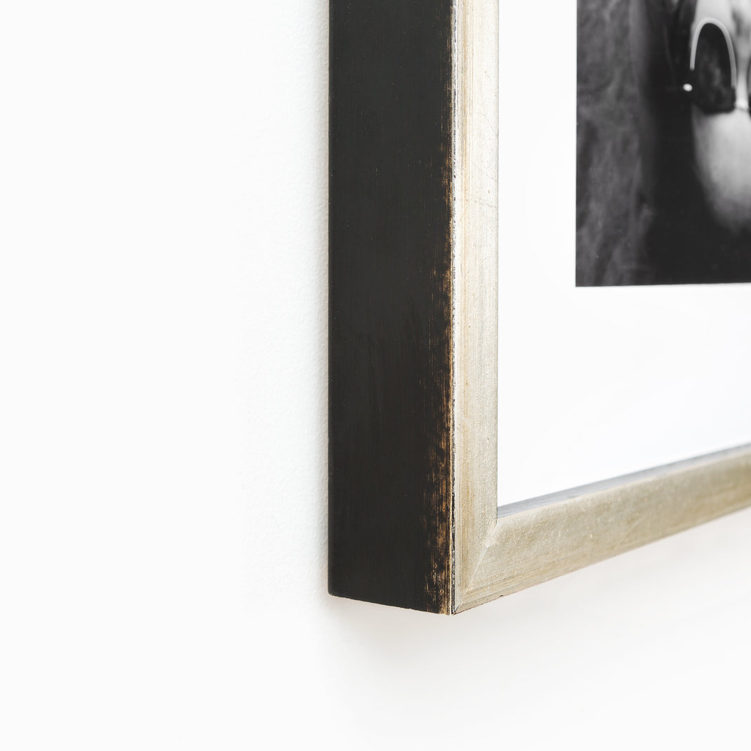 bottom left corner of Black & white photo of a woman wearing sunglasses on the beach framed in a silver Beverly frame with white mat