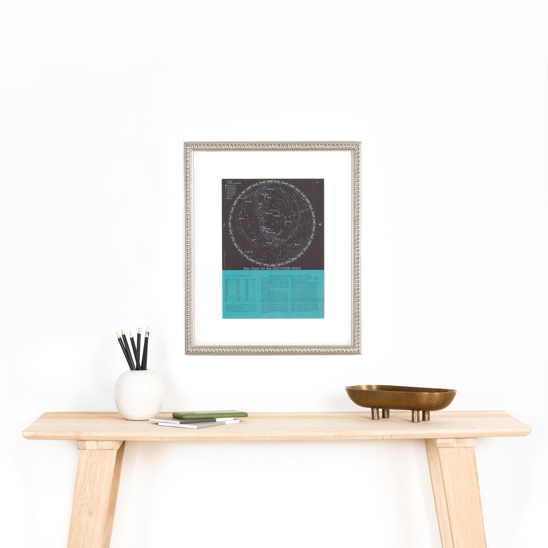star chart of the southern skies framed in Dover silver frame with wave detail hanging on a white wall above wooden console table