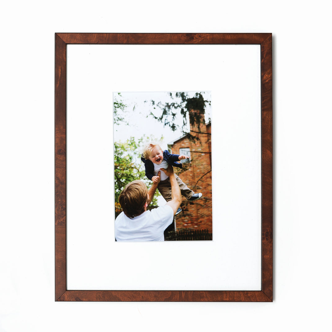photo of a dad throwing his son in the air framed in skinny dark burl wood Frederick frame with a white mat