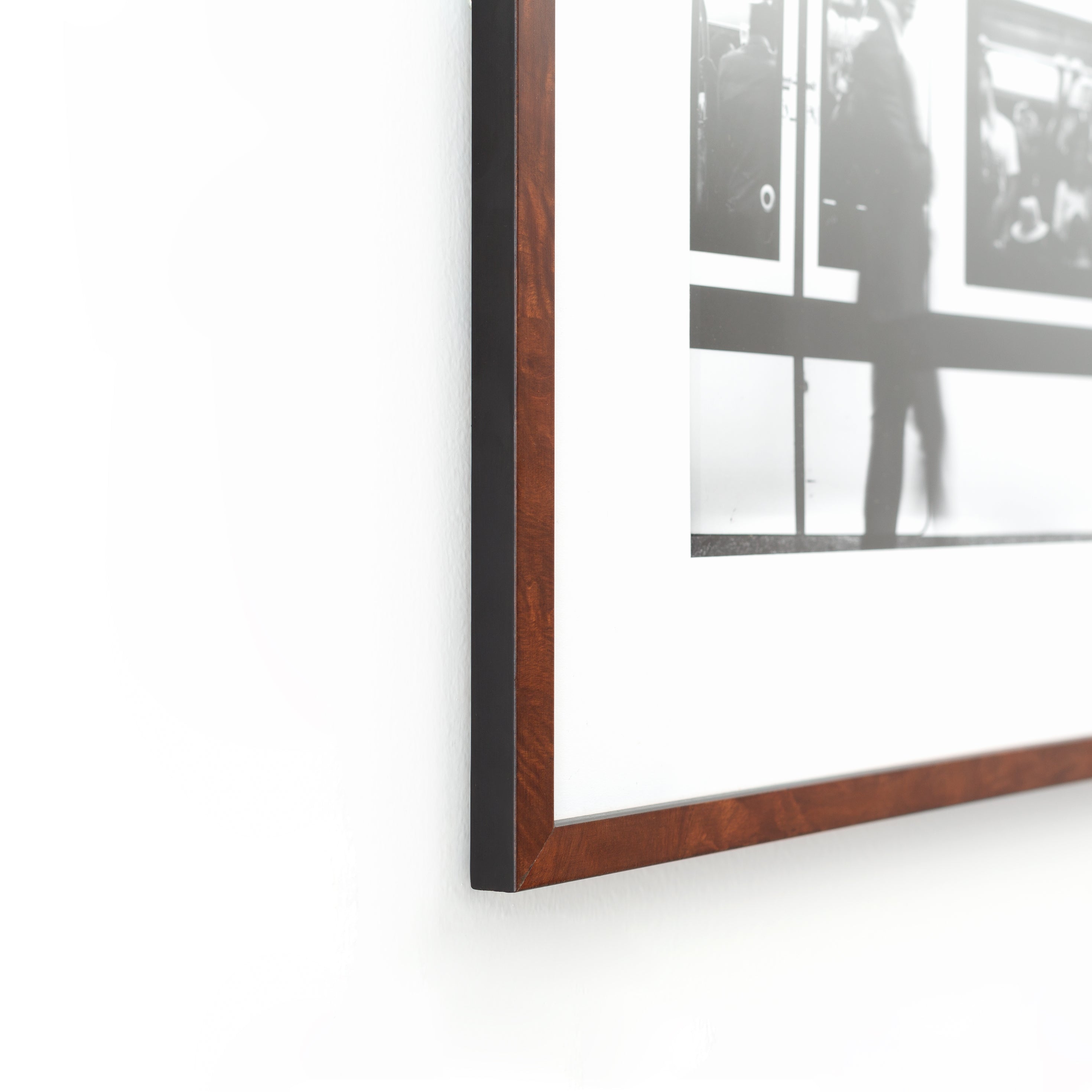 bottom left corner of blurry black and white photo of a man in front of a subway train framed in dark skinny burl wood Frederick frame with a white mat