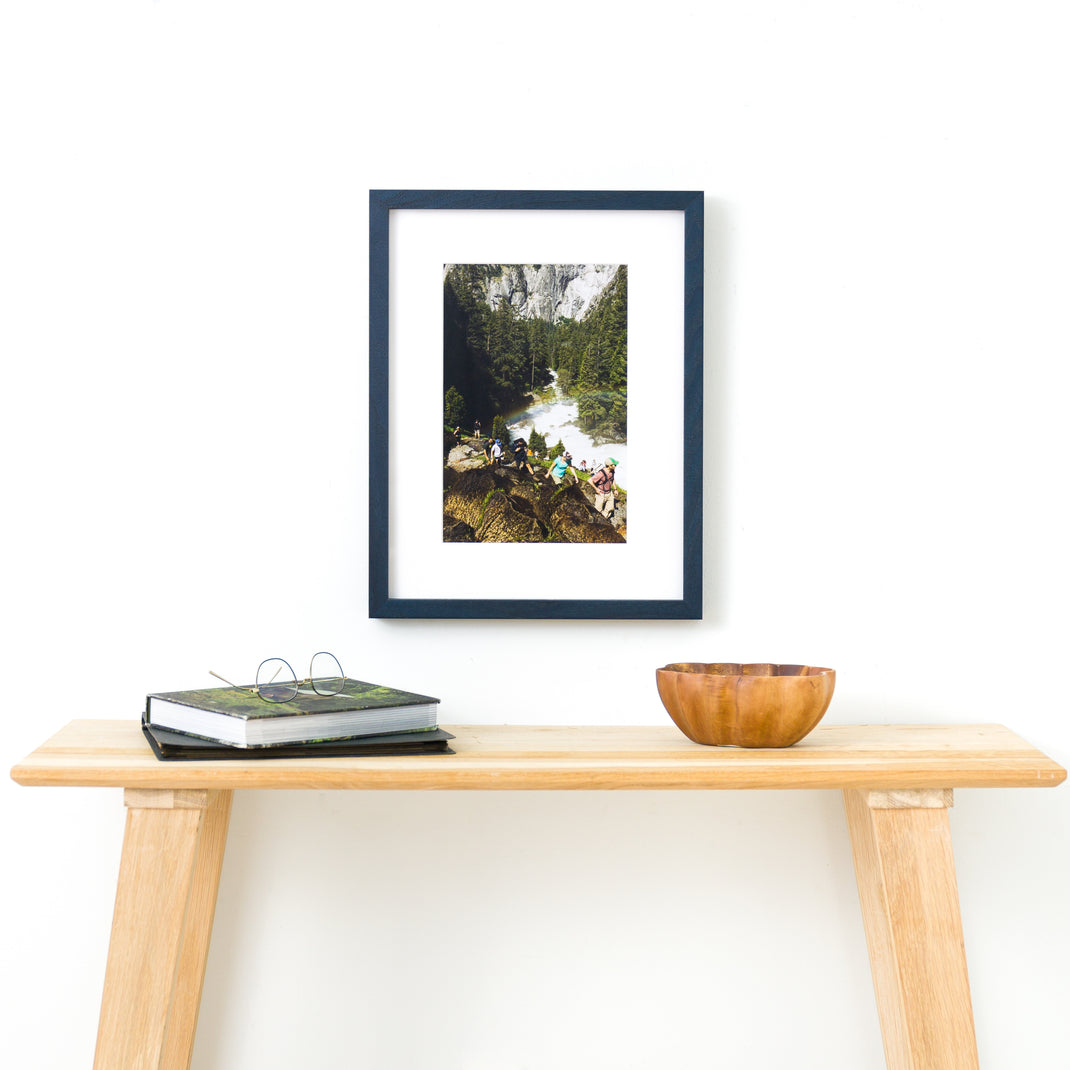 photograph of hikers framed in Indigo Walnut frame with white mat hanging on a white wall above a wood console table