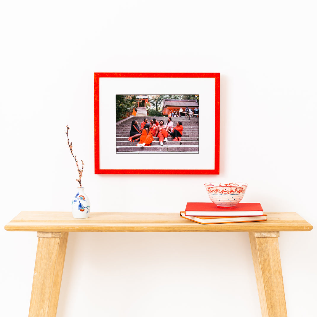 photograph of girls sitting on steps in Kyoto red glazed frame with a white mat hanging on a white wall above a wood console table