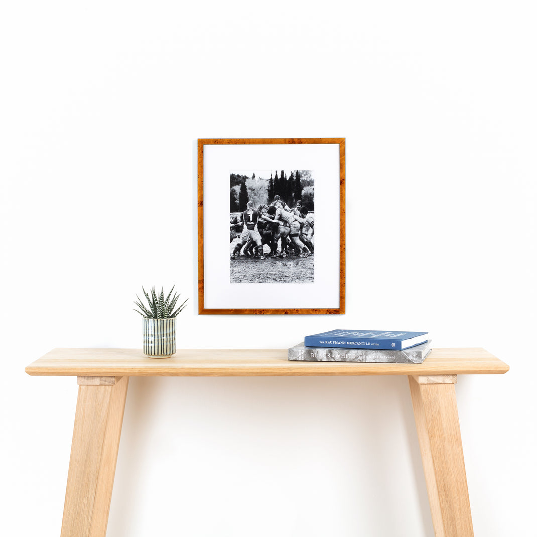 vintage black and white rugby photo framed in thin honey burl wood Lawrence frame with a white mat hanging on a white wall above a wood console table