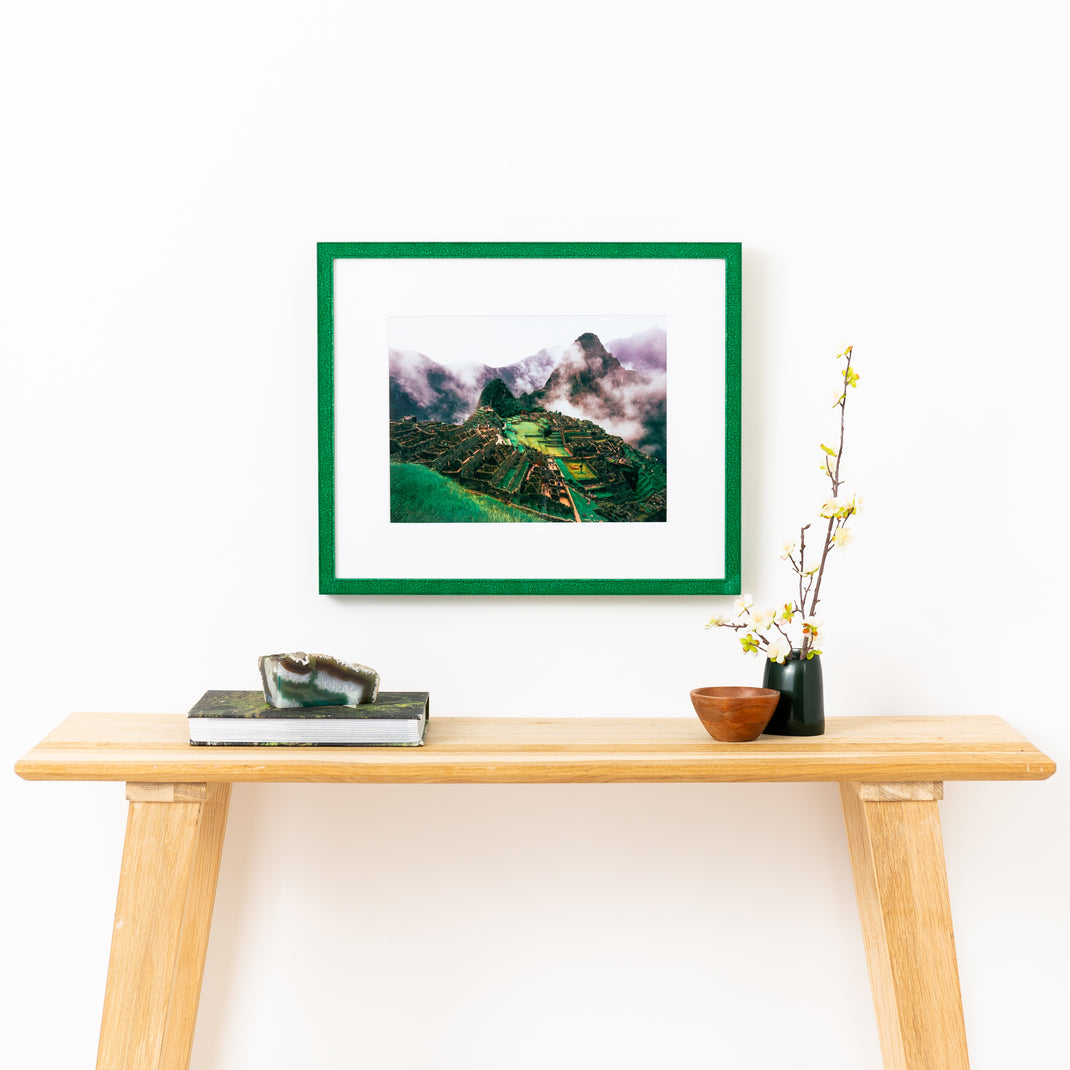 photograph of Machu Picchu framed in glazed emerald green Lima frame with a white mat hanging on a white wall above a wood console table