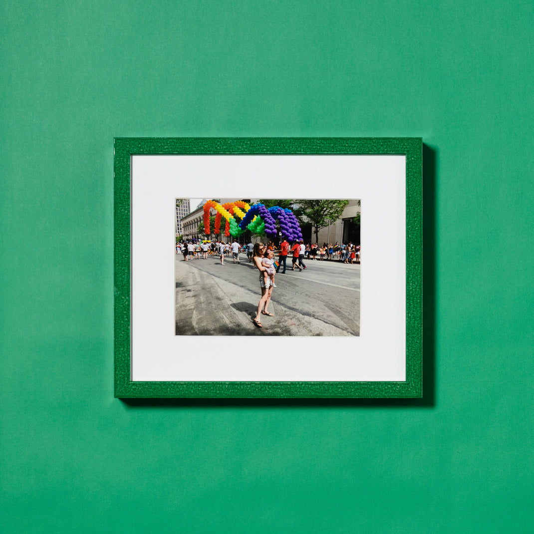 Pride parade photo framed in framed in glazed green Lima frame hanging on a green wall