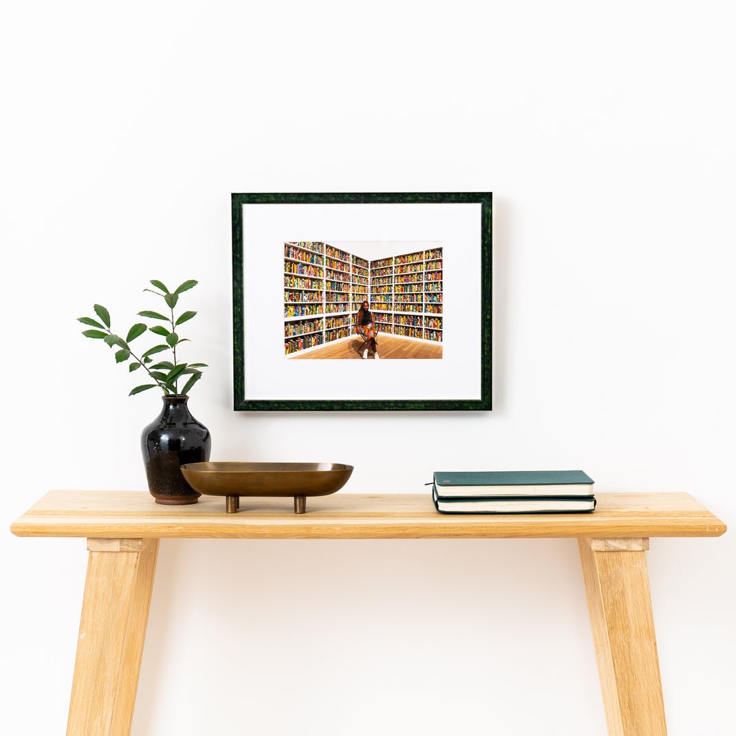 photograph of woman in front of books framed in London green glazed frame with a white mat hanging on a white wall above a wood console table
