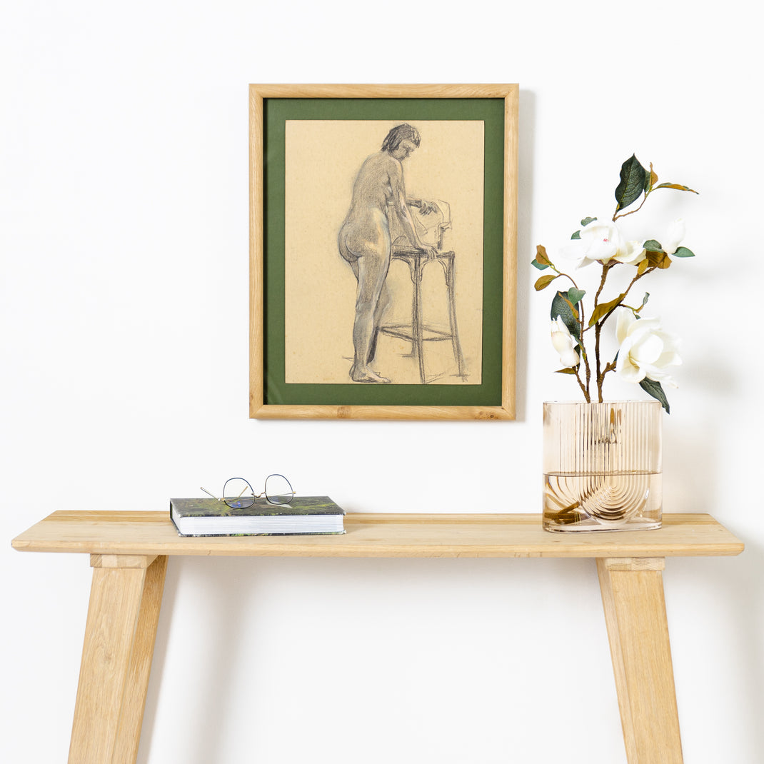 charcoal figure drawing framed in rounded burl wood frame with a green mat hanging on a white wall above a wood console table