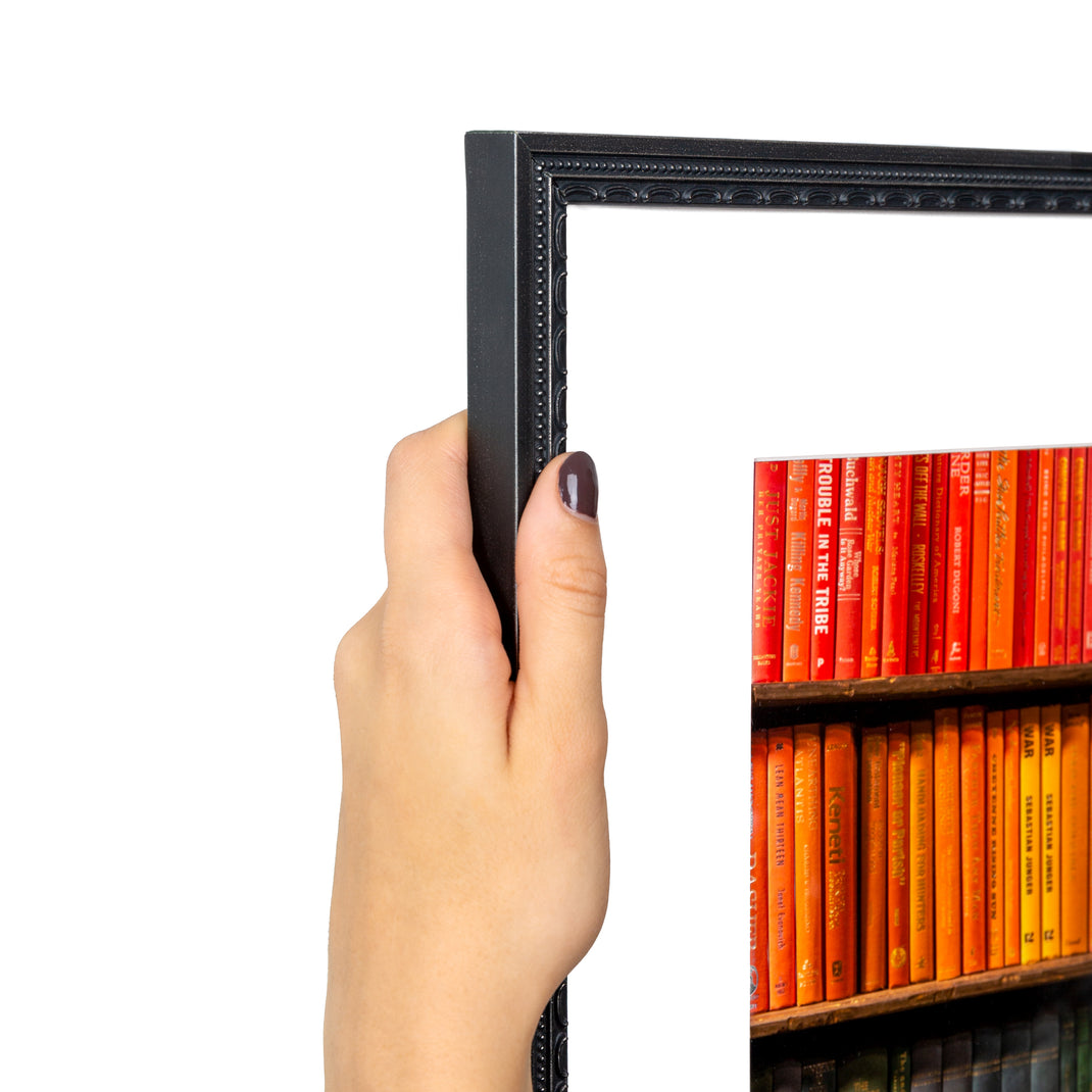 top left corner of photograph of a bookshelf arranged in rainbow framed in detailed black frame with a white mat