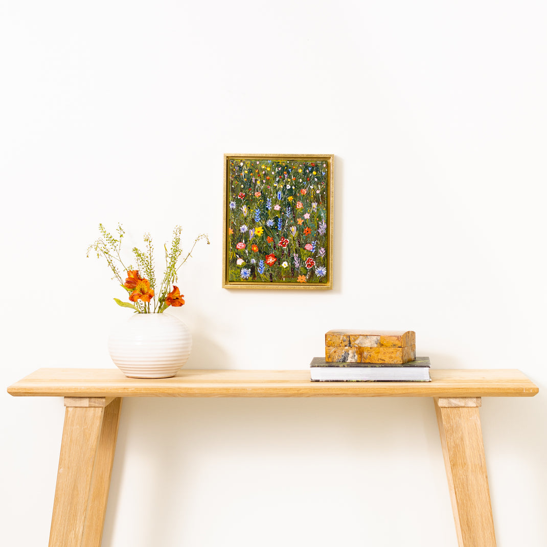 painting of wildflowers on canvas framed in Quito gold canvas floater frame hanging on a white wall over a wood console table
