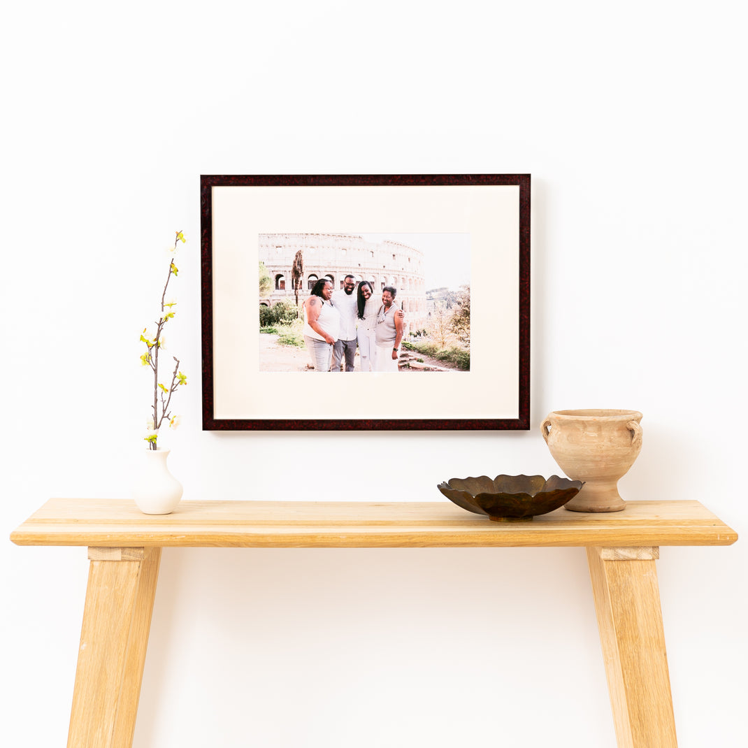 photo of group in front of the Colosseum framed in deep burgundy glazed Rome frame with a white mat hanging on a white wall above a wood console table