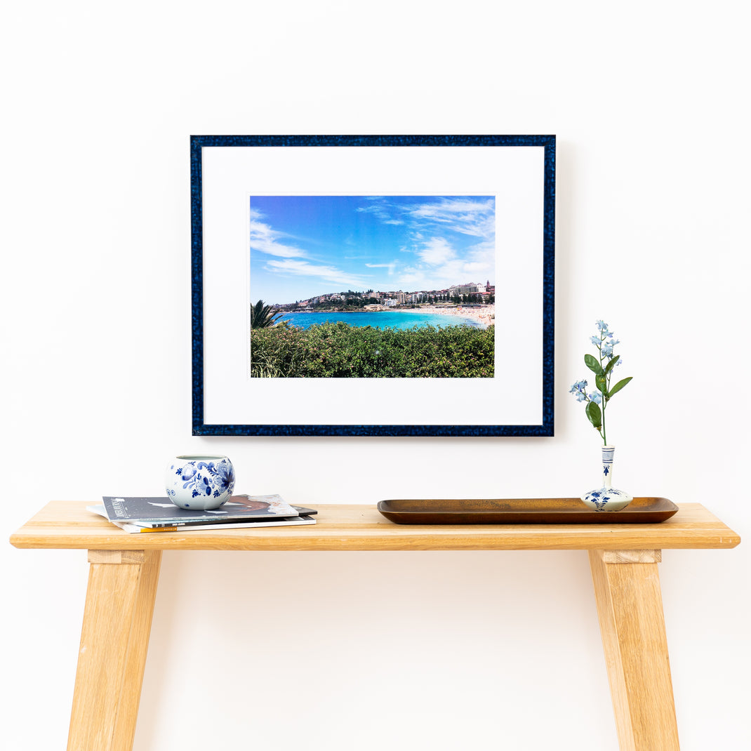 landscape photo framed in deep blue glazed Sydney frame with a white mat hanging on a white wall above a wood console table