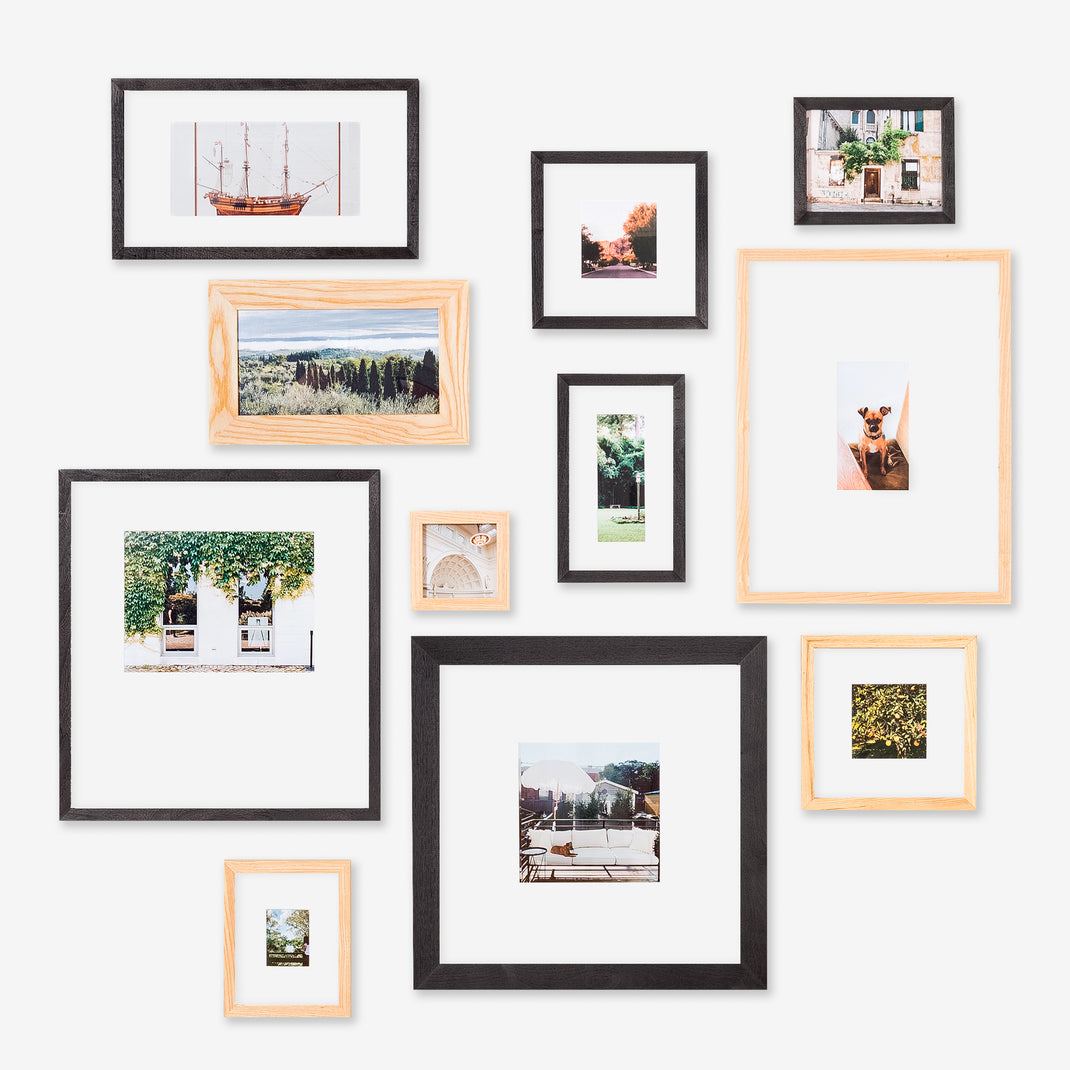 A styled gallery wall arrangement of multiple picture frames in black and light natural wood, each holding a different landscape or lifestyle photograph, mounted on a clean white wall.