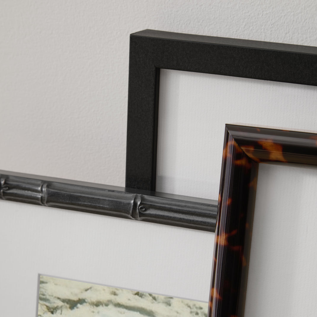 Closeup details of black walnut and tortoiseshell frames leaning against a wall