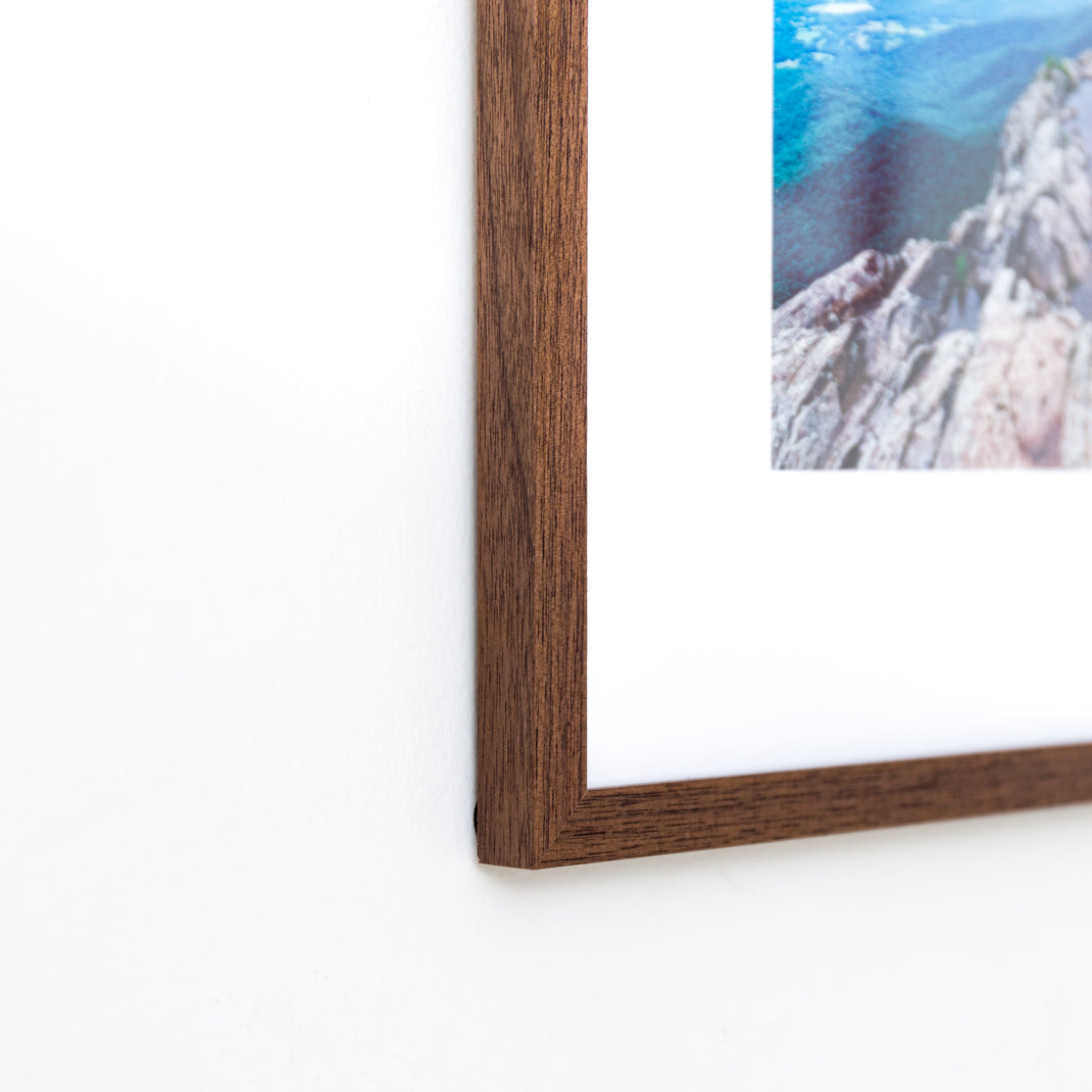 bottom left corner of landscape photo of mountains framed in mini Walnut hardwood frame style with a white mat