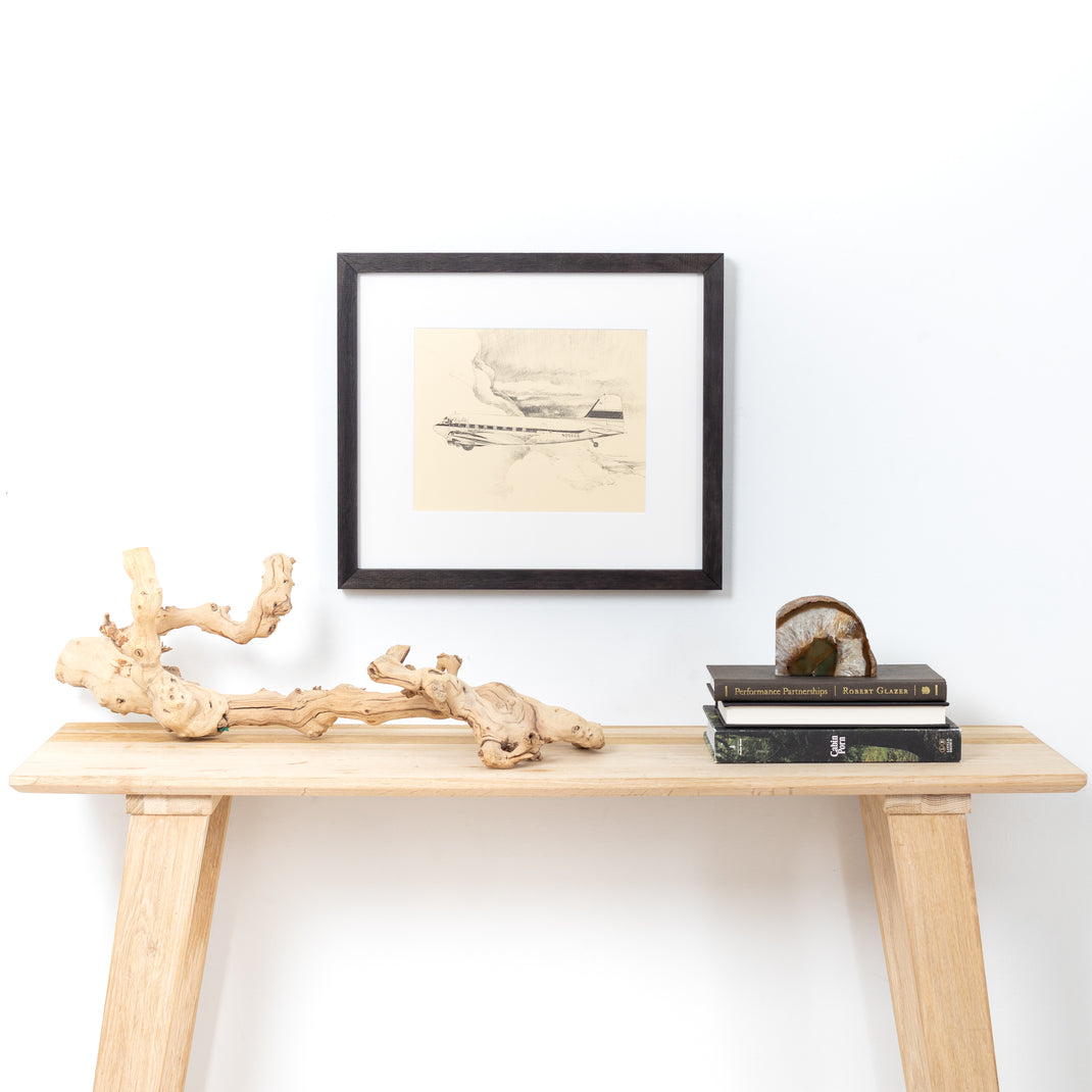 Black and white sketch of an airplane framed in Black Walnut Gallery frame with a white mat hanging on a white wall above a wood entry table