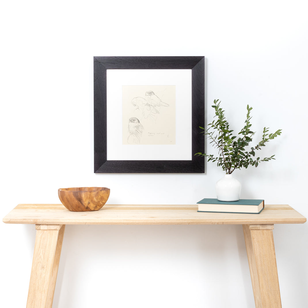 black and white sketch of birds framed in Black Walnut Wide frame with white mat hanging on a white wall over a wood entry table