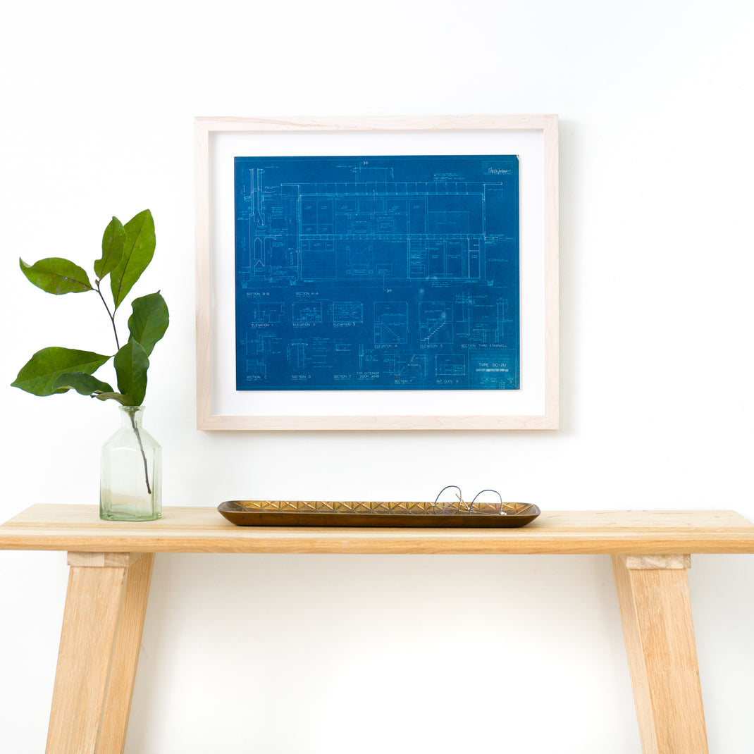 architectural blueprint framed in bleached maple gallery frame hanging on a white wall above wood console table