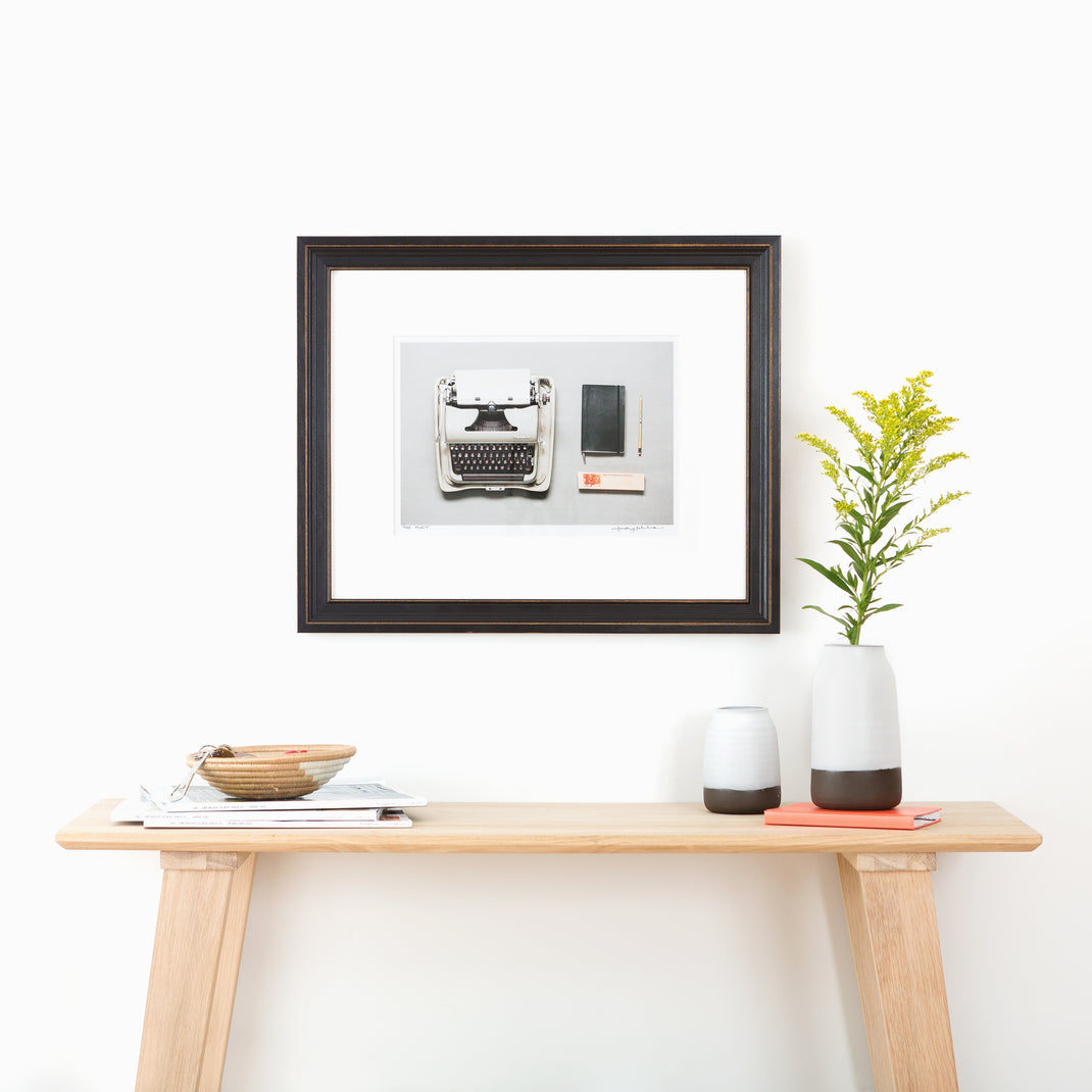 Photo of a typewriter framed in Augusta wide distressed black frame with white mat hanging on a white wall above an entry table