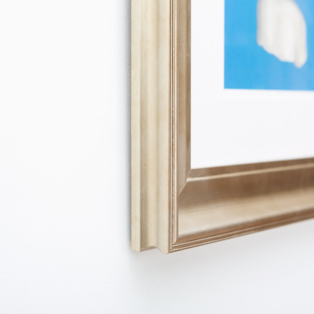 bottom left corner of an art print of a woman's print on a blue background framed in bowery wide sloped silver frame