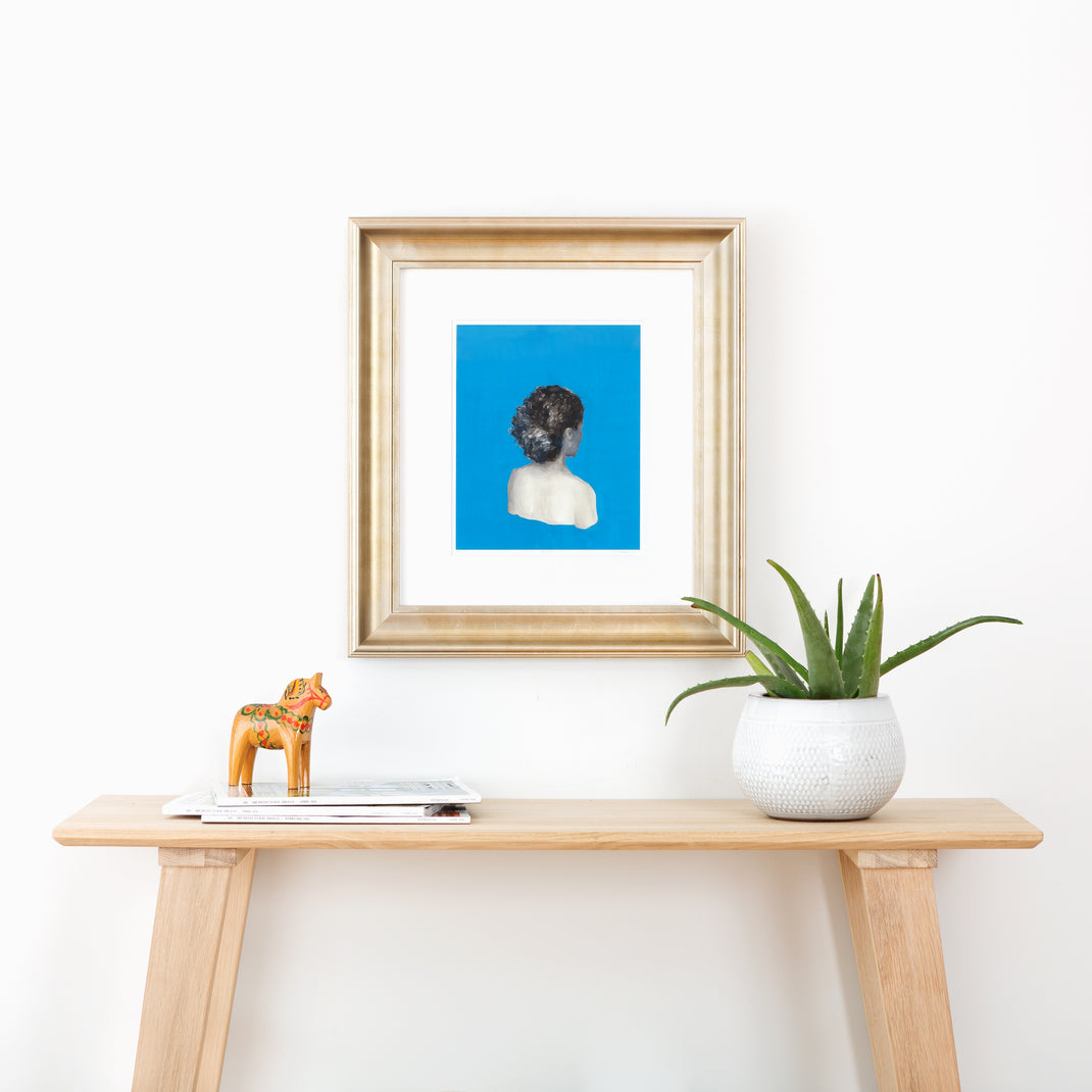 art print of a woman's print on a blue background framed in bowery wide sloped silver frame hanging on a white wall over a wooden console table