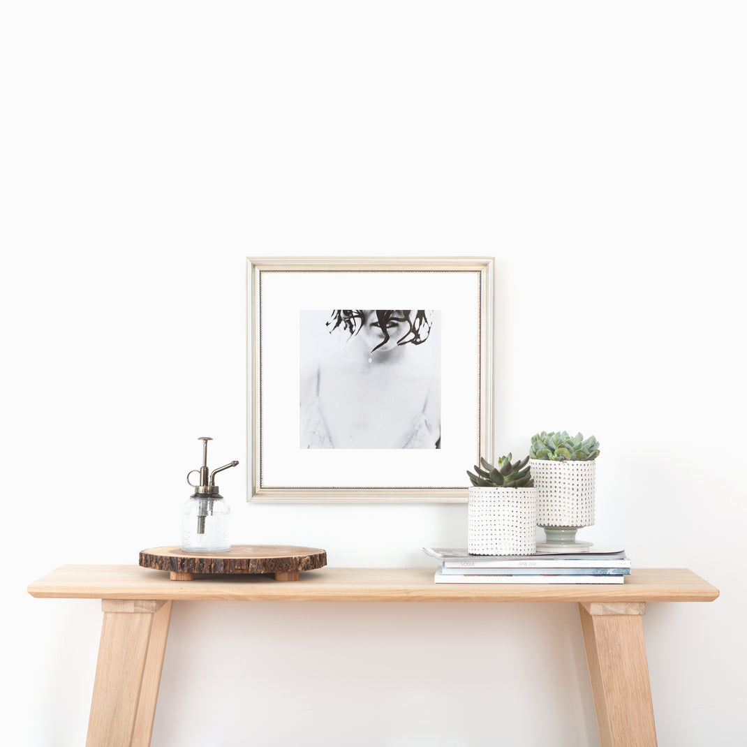 black and white photo of a woman framed in Buckhead silver beaded frame with white mat hanging on a white wall above a wooden console table