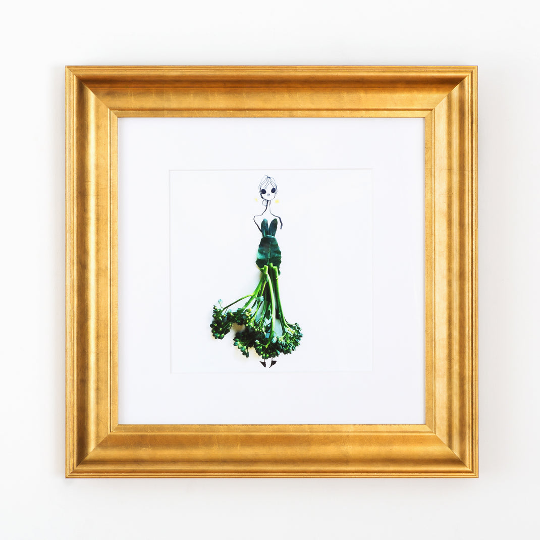 illustration of a woman with a broccolini skirt framed in wide sloped gold Chelsea frame with a white mat