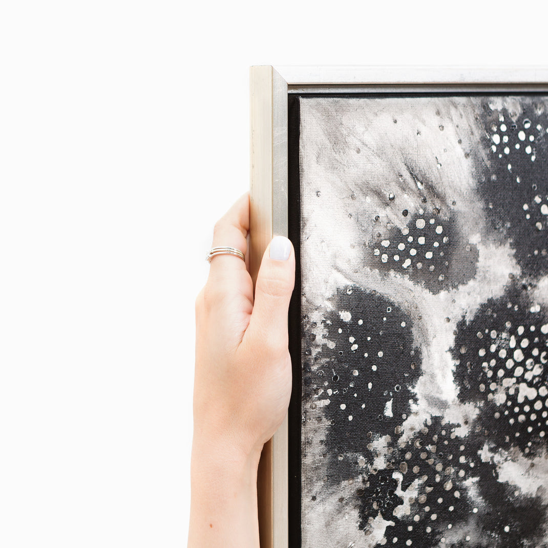 top left corner of black and white canvas painting framed in Gatwick, a silver floater canvas frame