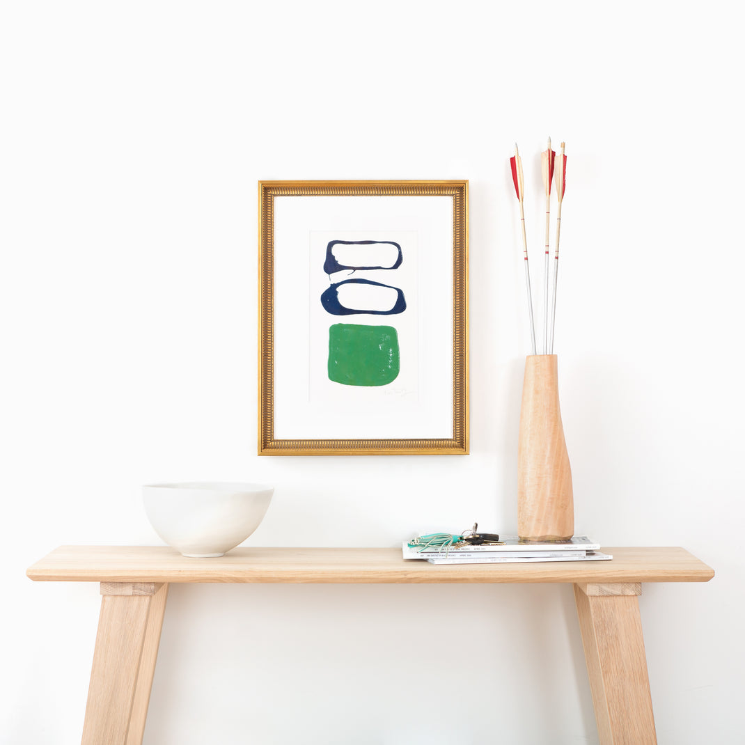abstract blue and green art framed in antique fluted gold Georgetown frame with a white mat hanging on a white wall above a wood console table