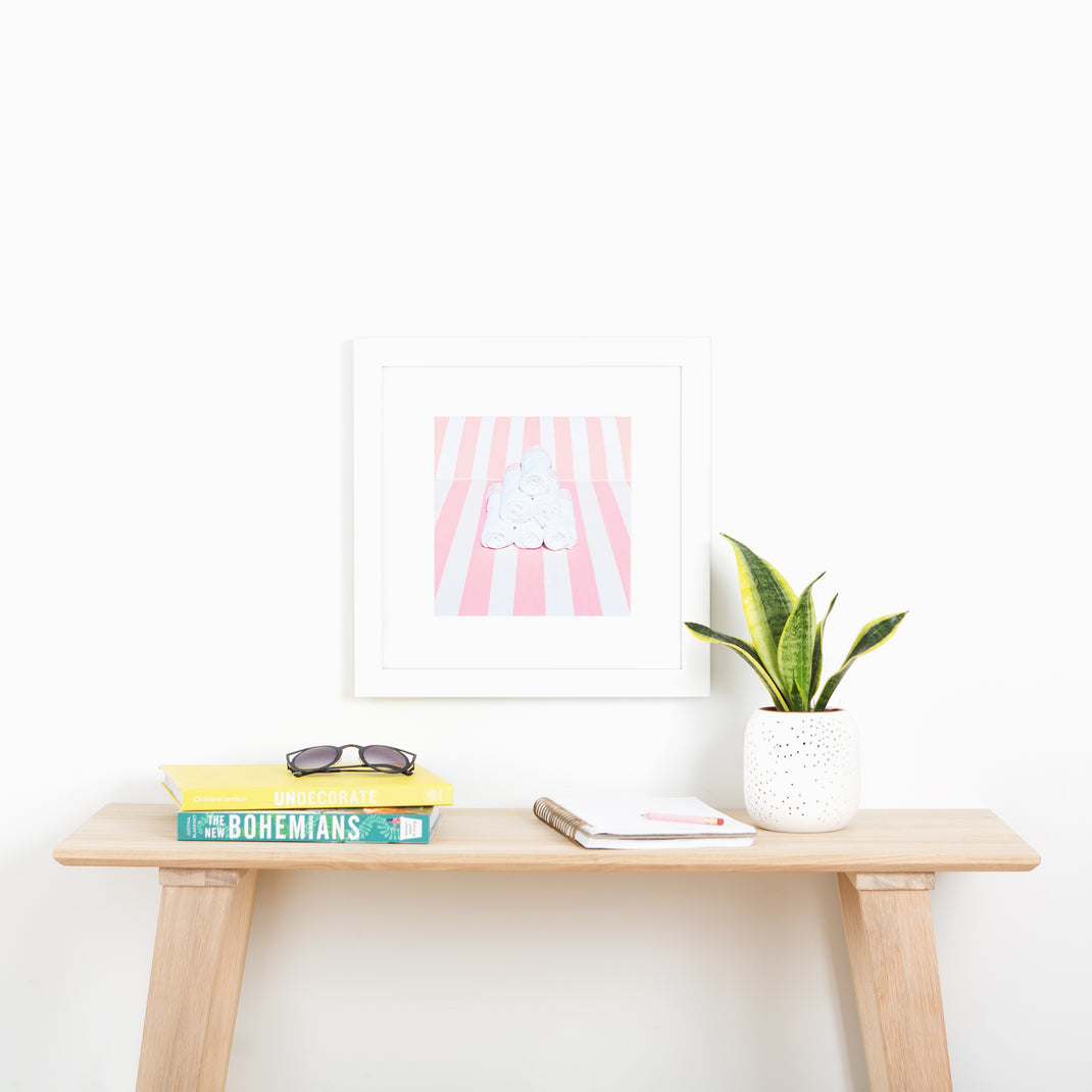 Photo of towels on a pink striped beach chair framed in modern white Irvine frame with a white mat hanging on a white wall above a wood console table