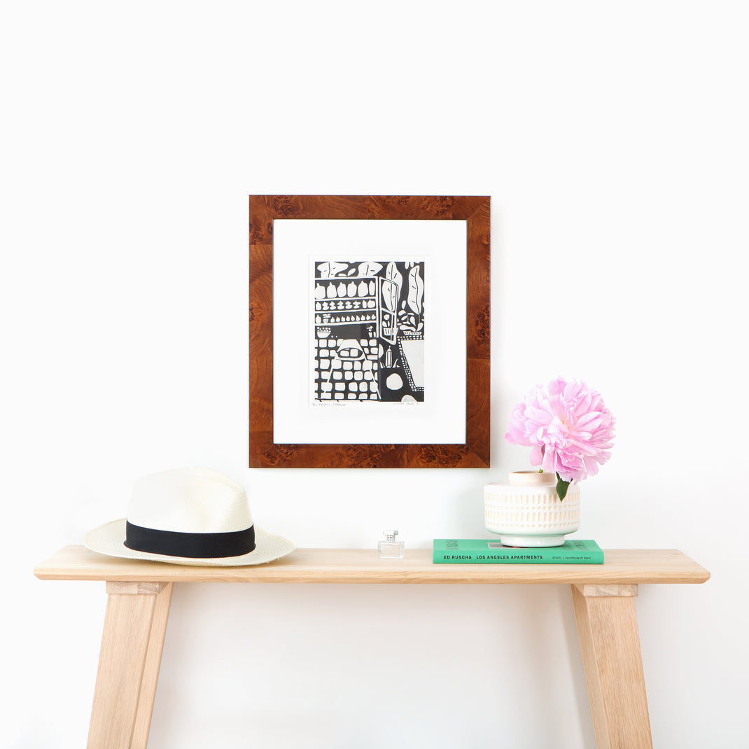 black and white linocut print framed in Jambi tiger wood frame with white mat hanging on a white wall above a wood console table