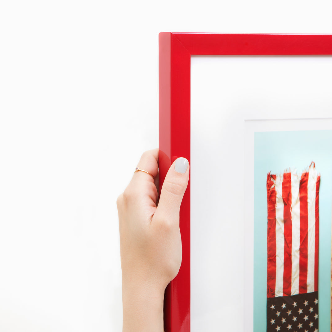 top left corner of flat lay photograph of outdoor equipment framed in red lacquered Madrid frame with a white mat