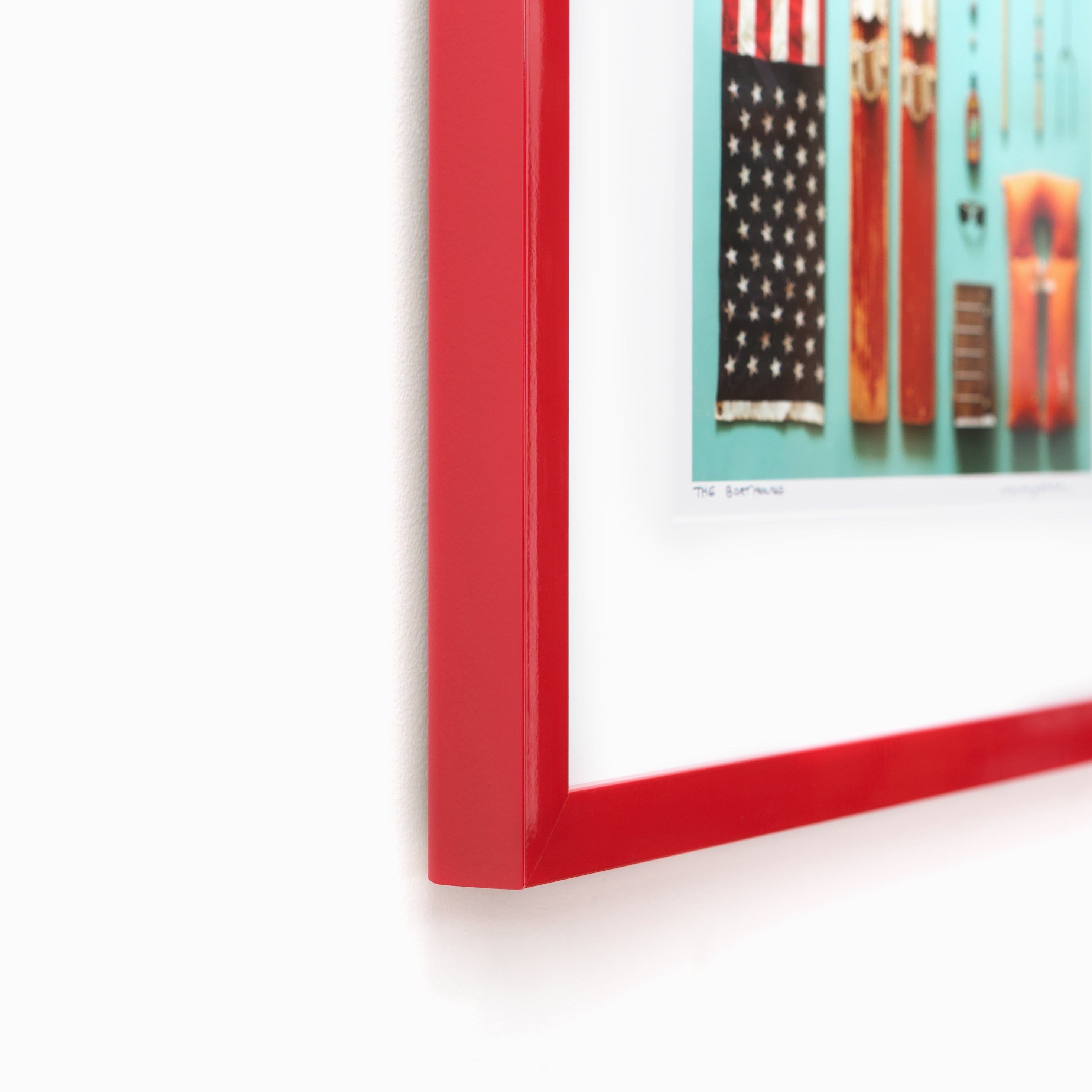 bottom left corner of flat lay photograph of outdoor equipment framed in red lacquered Madrid frame with a white mat