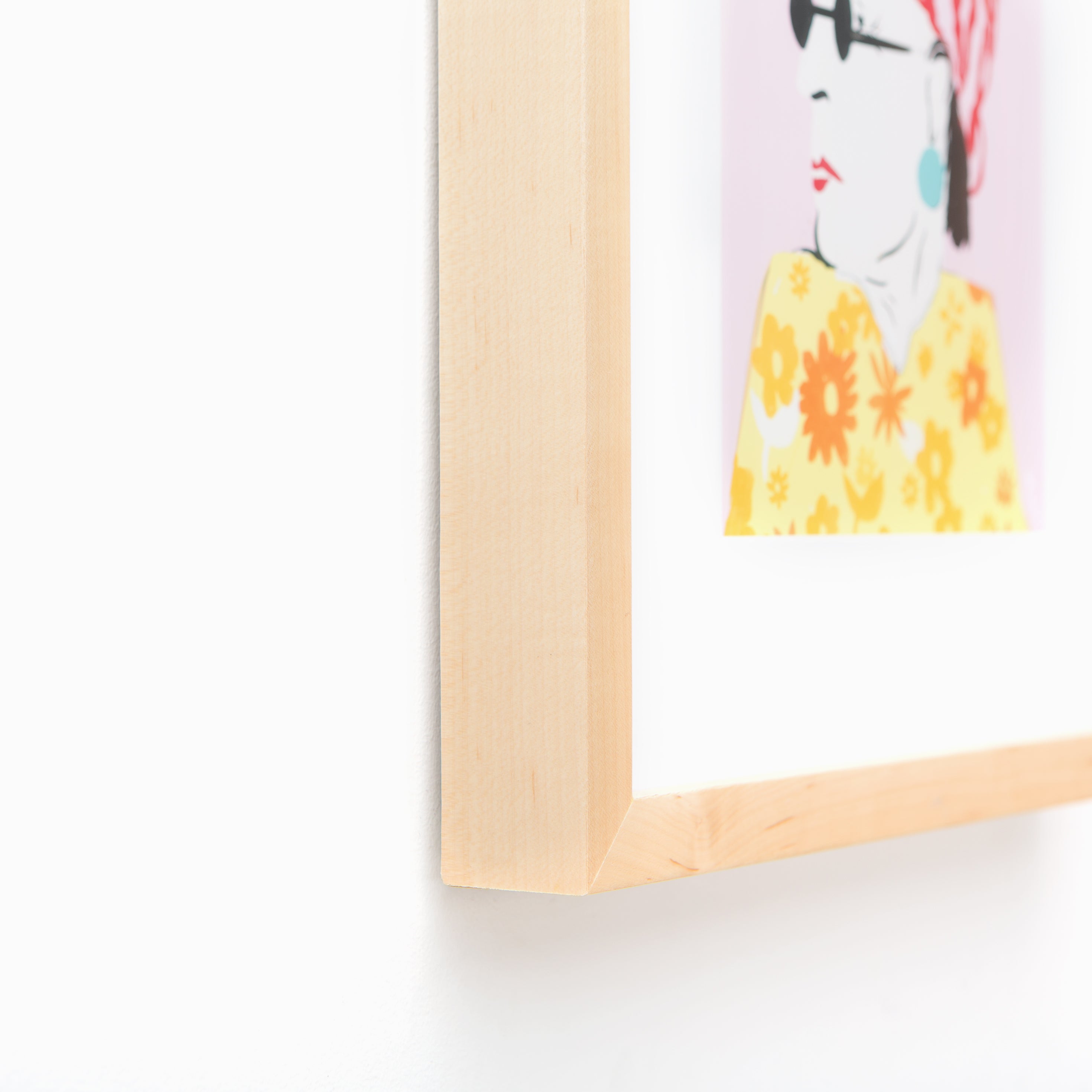 bottom left corner of illustrated portrait of a woman in a floral dress framed in light wood Marin frame