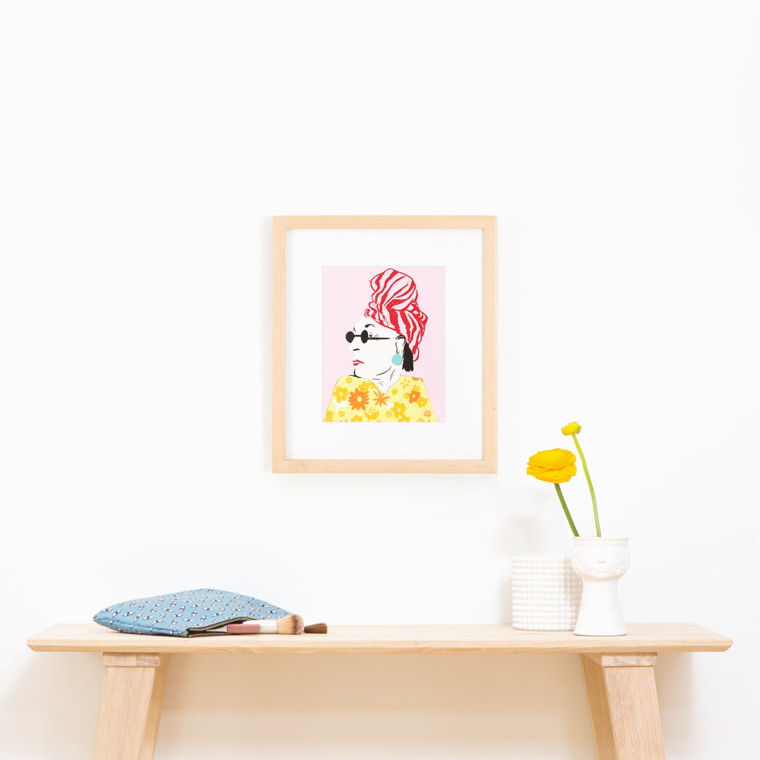 illustrated portrait of a woman in a floral dress framed in light wood Marin frame hanging on a white wall above a wood console table