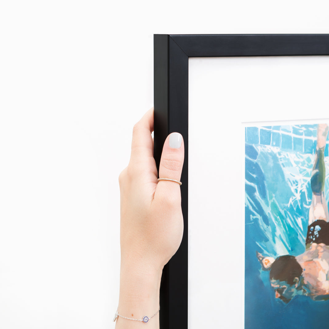 top left corner of art print of a man swimming in a pool framed in thin black gallery Mercer Slim frame with a white mat