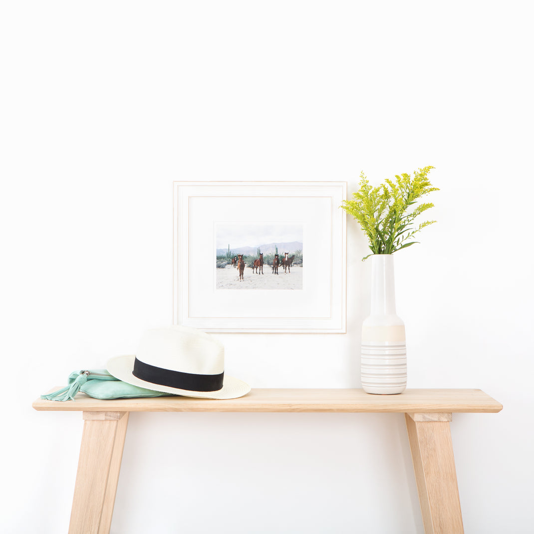 photograph of horses in the desert framed in wide distressed Montauk frame with a white mat hanging on a white wall above wood console table