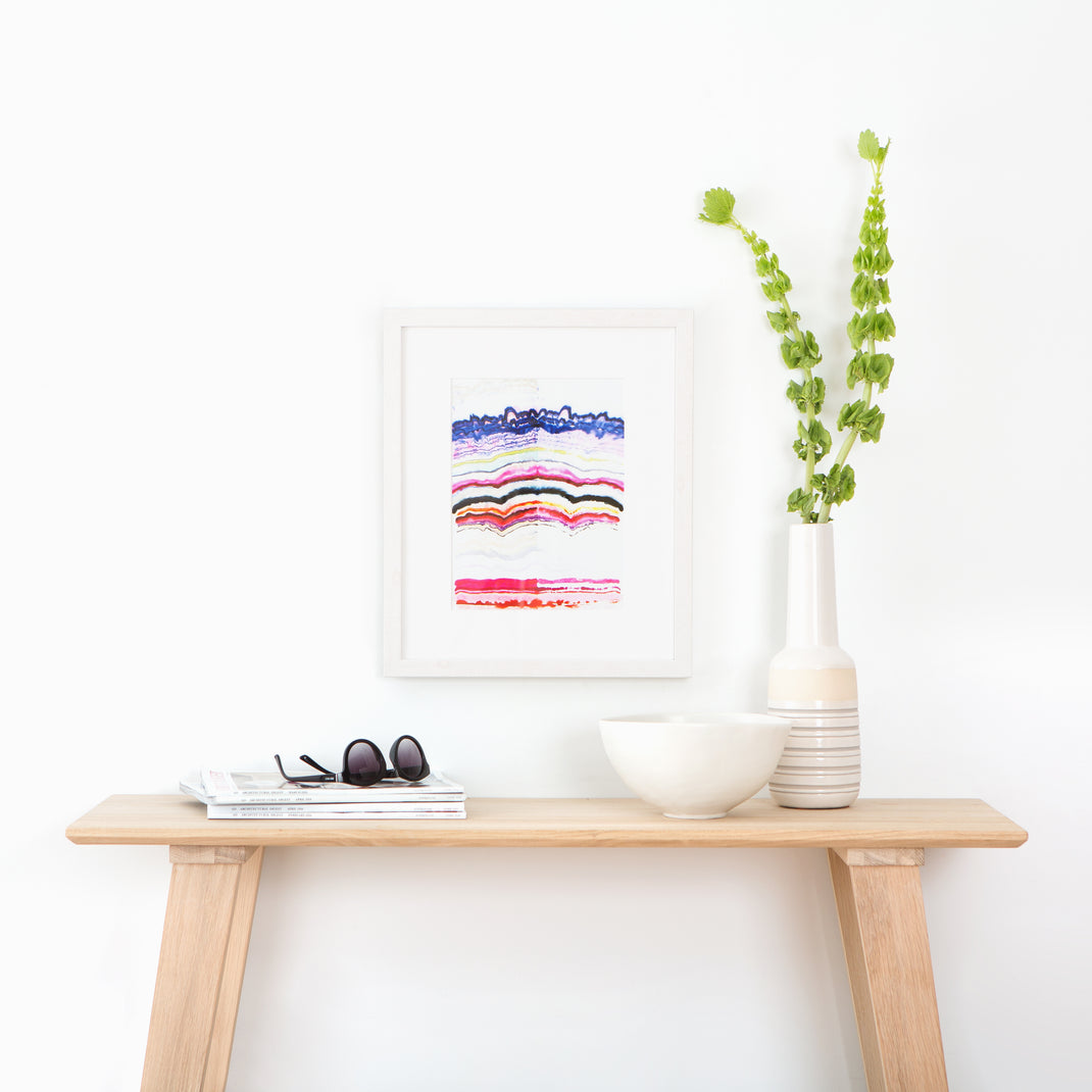 colorful abstract line art framed in whitewashed gallery Monterey frame hanging on a white wall above a wood console table