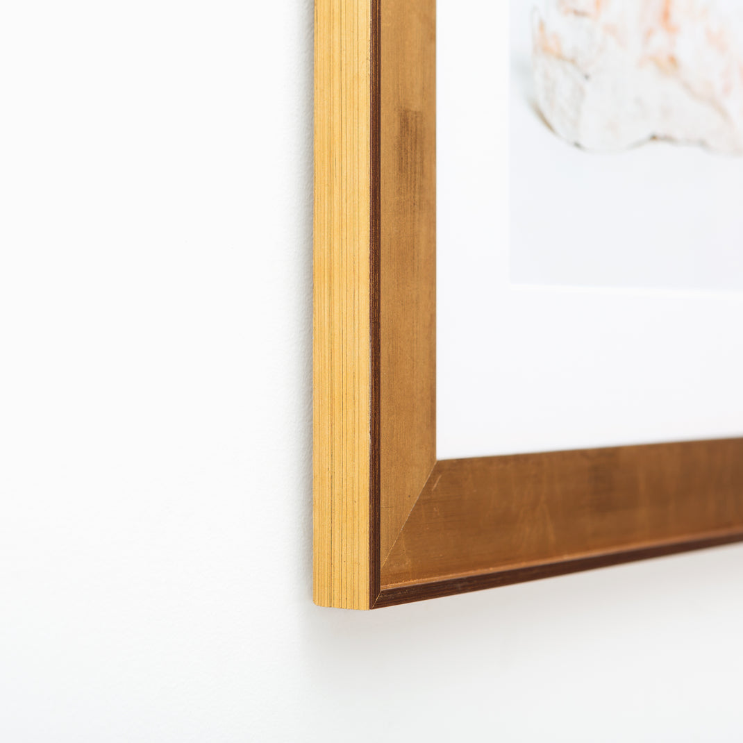 bottom left corner of pink geode framed in wide gold Potomac frame with a white mat