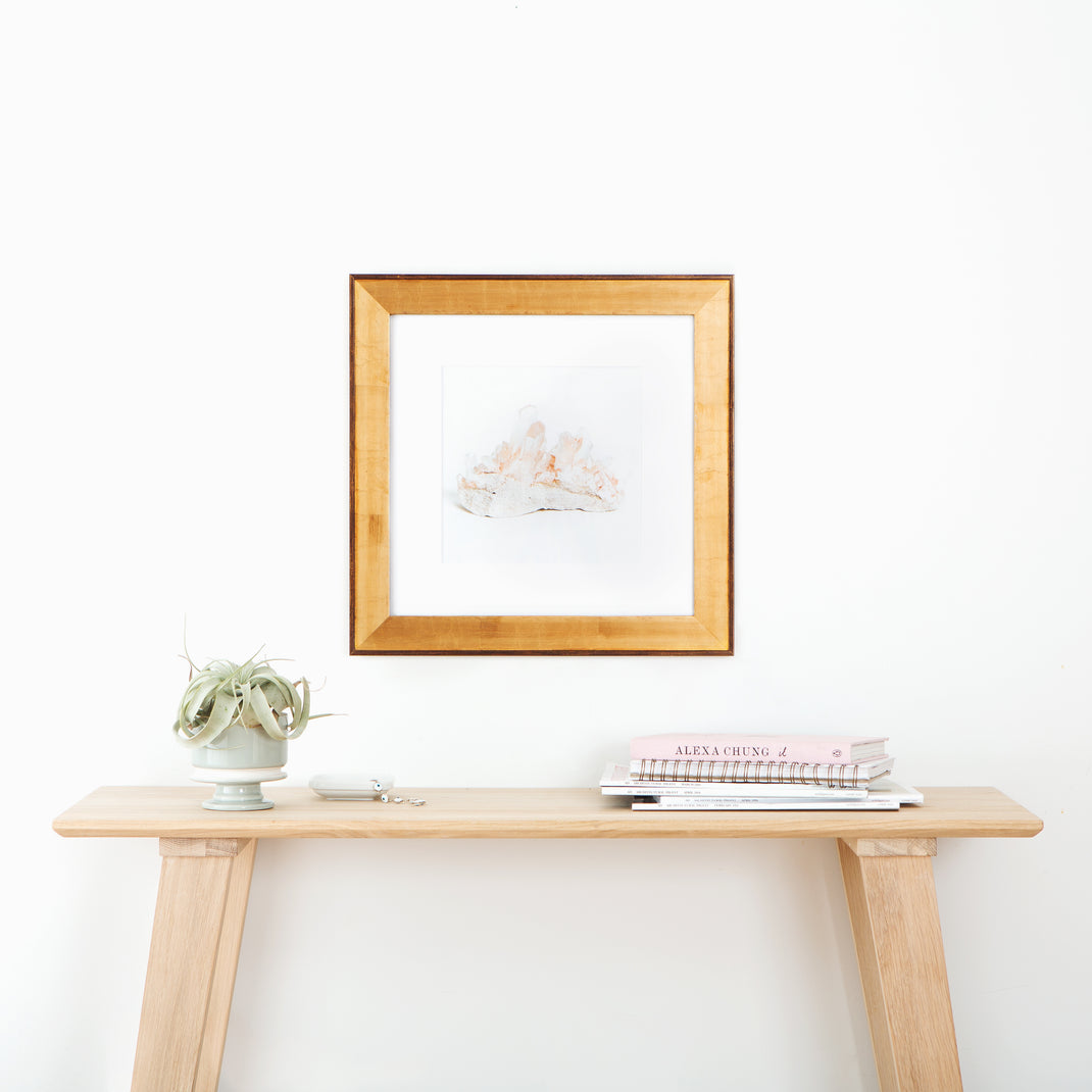 pink geode framed in wide gold Potomac frame with a white mat hanging on a white wall above a wood console table